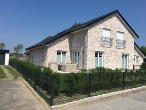 Ein zweistöckiges Haus mit Backsteinfassade, einem Balkon mit Metallgeländer und einem gepflasterten Auffahrt.