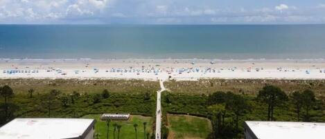 A view of a beach with a parking lot and buildings in the foreground.