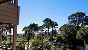 A view of a building with a balcony overlooking a landscape with trees and a distant view of a body of water. - Crashin' Waves-Oceanview w/new bikes, Chairs& King Bed (Hilton Head Island)