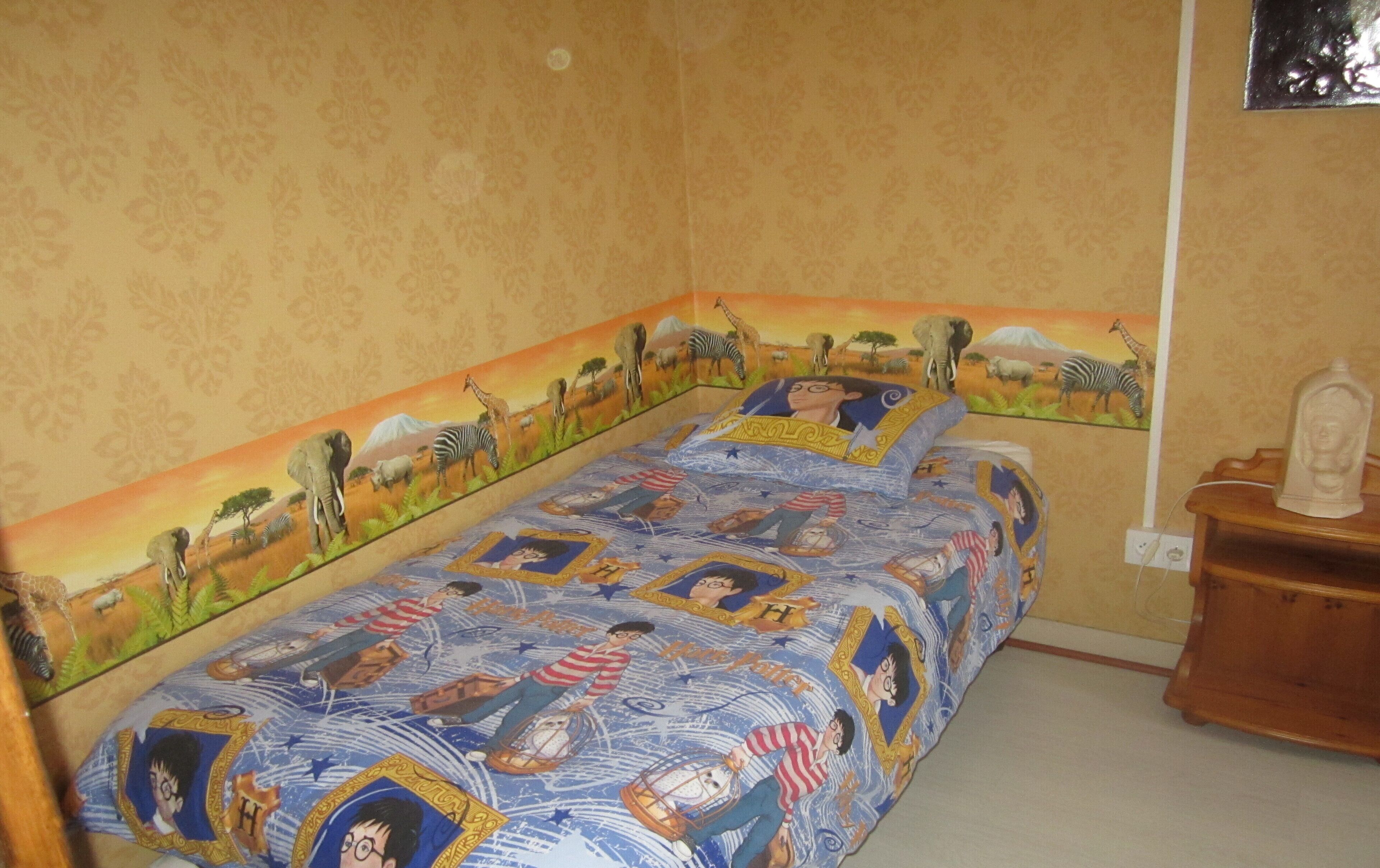 Ein Schlafzimmer mit einem Bett, das mit einem Harry-Potter-Duftüberzug, einem Nachttisch aus Holz und einer Wandlampe ausgestattet ist.