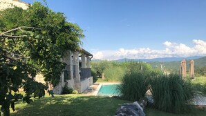 Ein Steinhaus mit Pool, umgeben von Grünflächen und Bergen im Hintergrund.