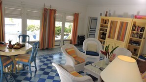 A room with a checkered floor, white wicker furniture, a dining table with fruit, and a bookshelf.