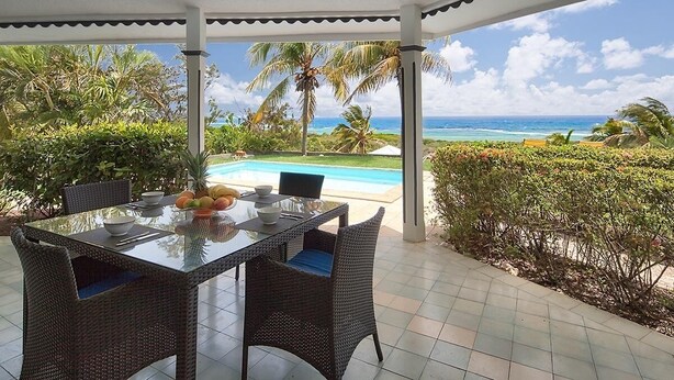 A covered outdoor dining area with a view of the ocean and a pool.