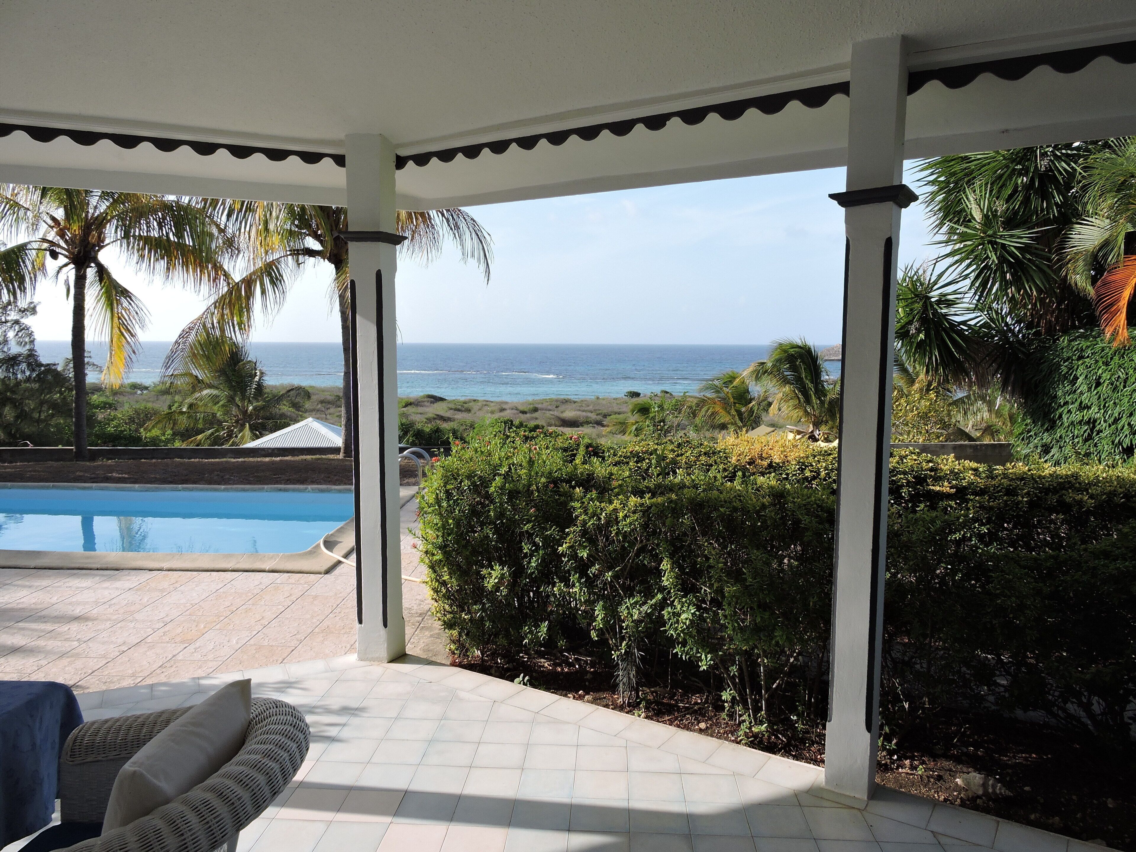 A covered outdoor area with a pool, seating, and a view of the ocean.