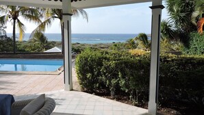A covered outdoor area with a pool, seating, and a view of the ocean.