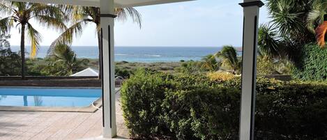 A covered outdoor area with a pool, seating, and a view of the ocean.