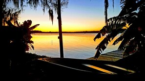 A sunset view from a dock with a calm body of water and palm trees.