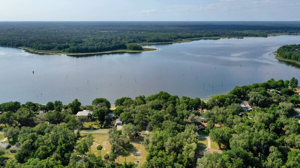 An aerial view of a lake surrounded by dense forest and residential areas with visible houses and roads.