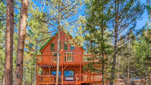 A two-story wooden cabin with a balcony, surrounded by trees.
