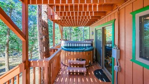 A wooden deck with a hot tub, a bench, and a door leading to an outdoor area.