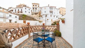 Une terrasse avec une table et des chaises, une vue sur des bâtiments blancs en arrière-plan et un sol carrelé en pierre.