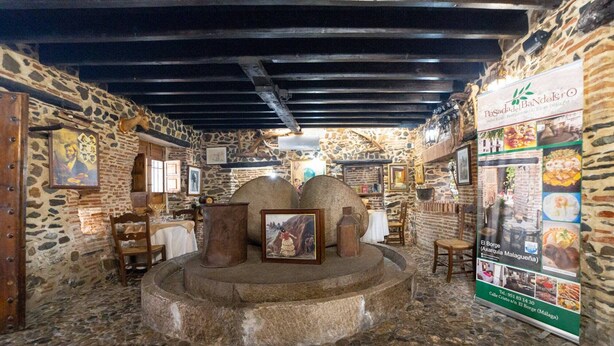 L’intérieur est de style rustique, avec des murs en pierre, des poutres en bois et une structure centrale également en pierre. Des tableaux encadrés ornent les murs, et un panneau affichant le menu se trouve sur le côté droit.