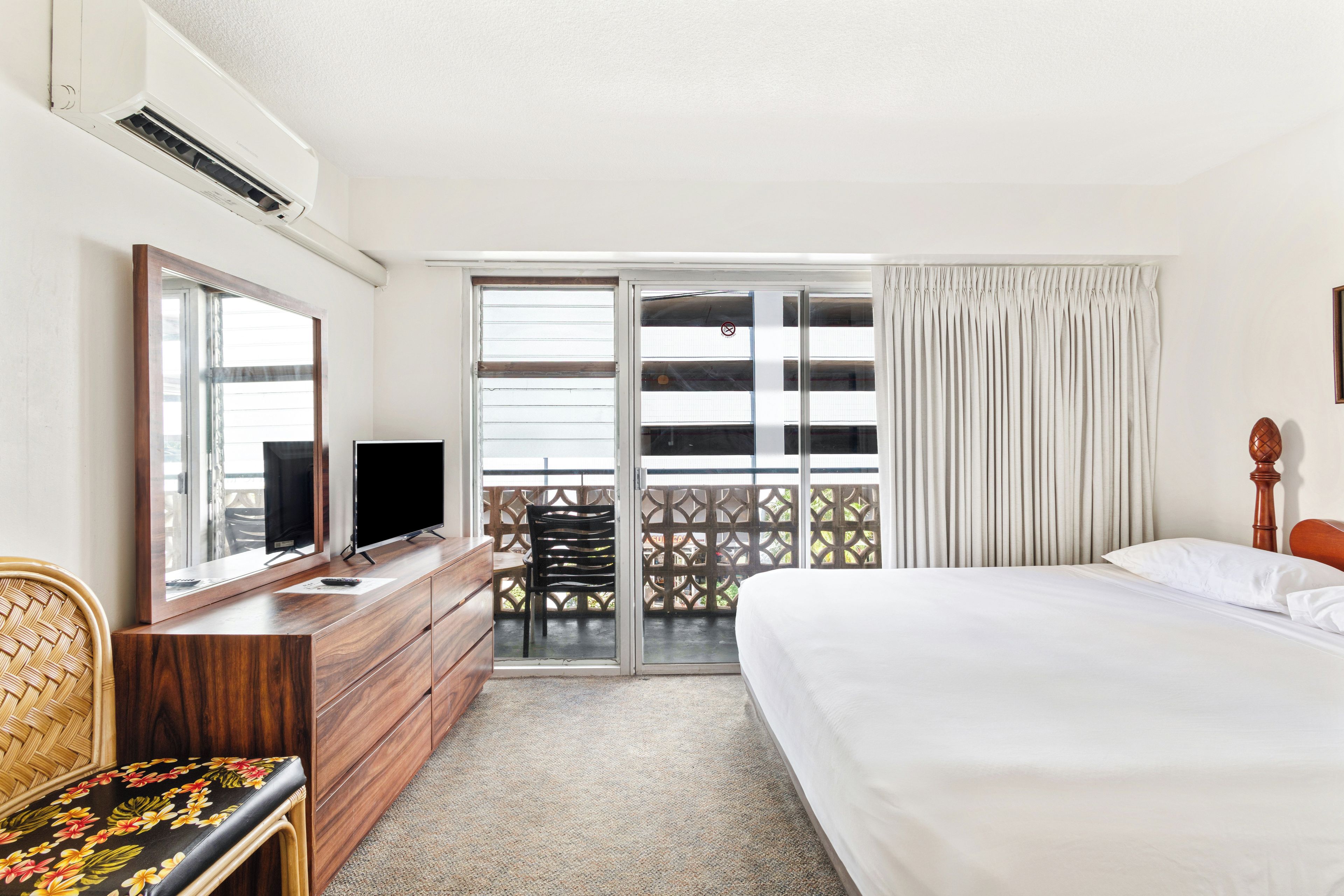A hotel room with a bed, a desk with a TV, a chair, and a balcony with a view.