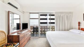 A hotel room with a bed, a desk with a TV, a chair, and a balcony with a view.