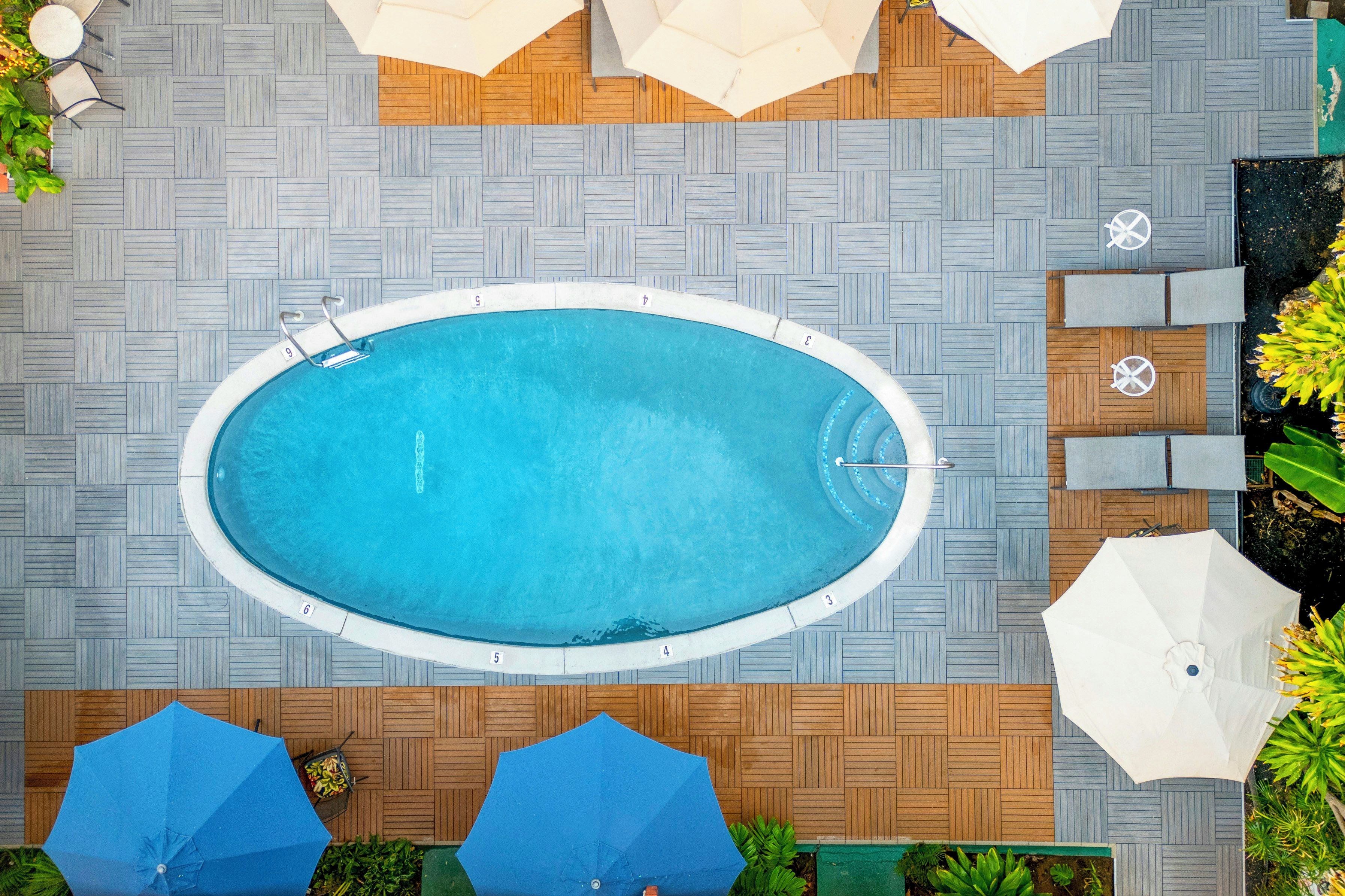 An oval-shaped pool with a wooden deck surrounding it, equipped with lounge chairs and umbrellas.