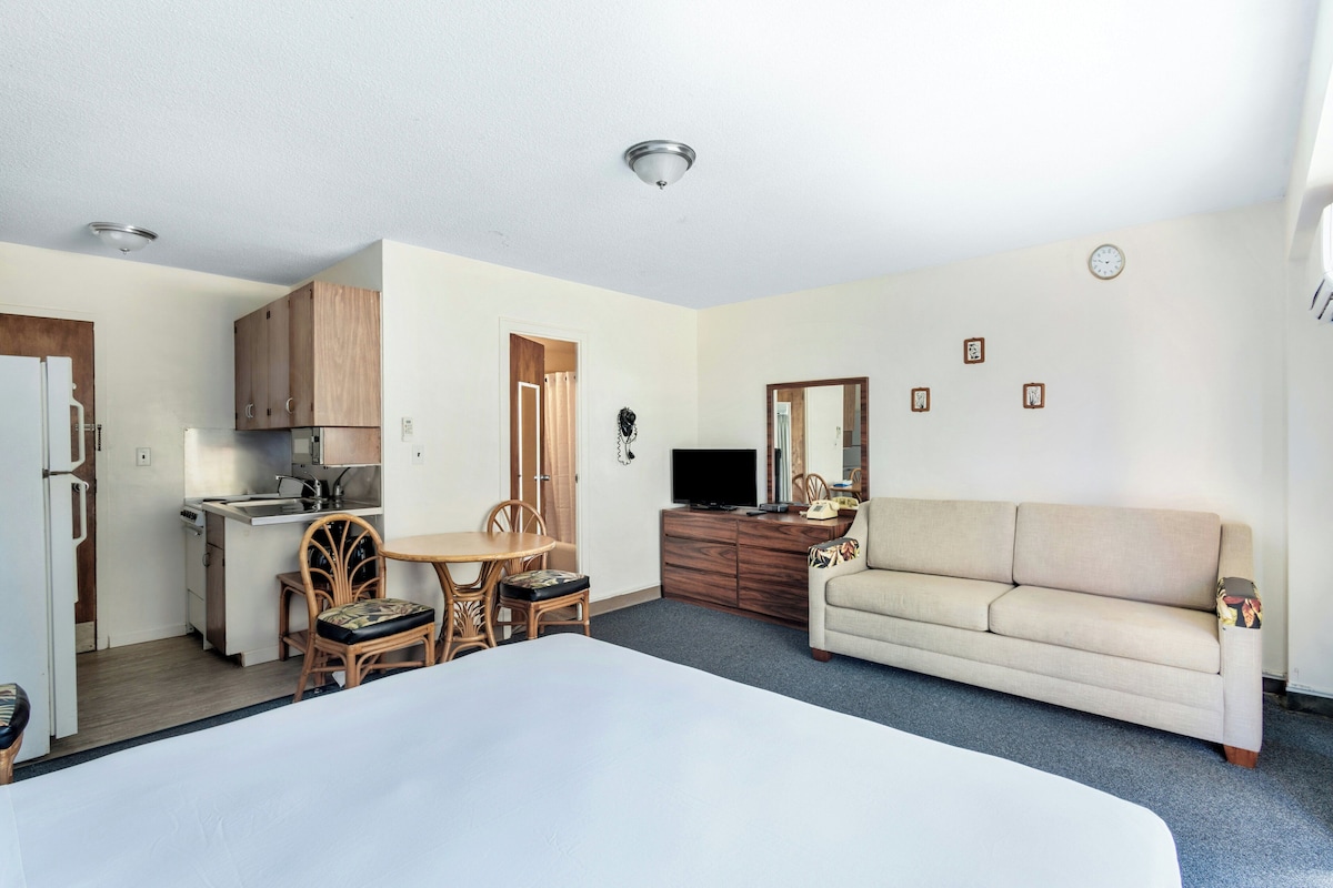 A compact room with a kitchenette, a dining area with a table and chairs, a sofa, and a television.