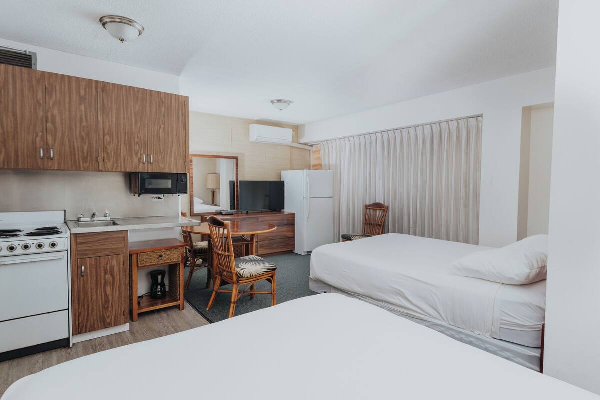 A hotel room with a kitchenette, a bed, a desk with a chair, and a television.
