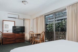 A hotel room with a bed, a TV on a wooden dresser, a dining table with chairs, and a balcony with curtains. - Royal Grove Waikiki (Honolulu)