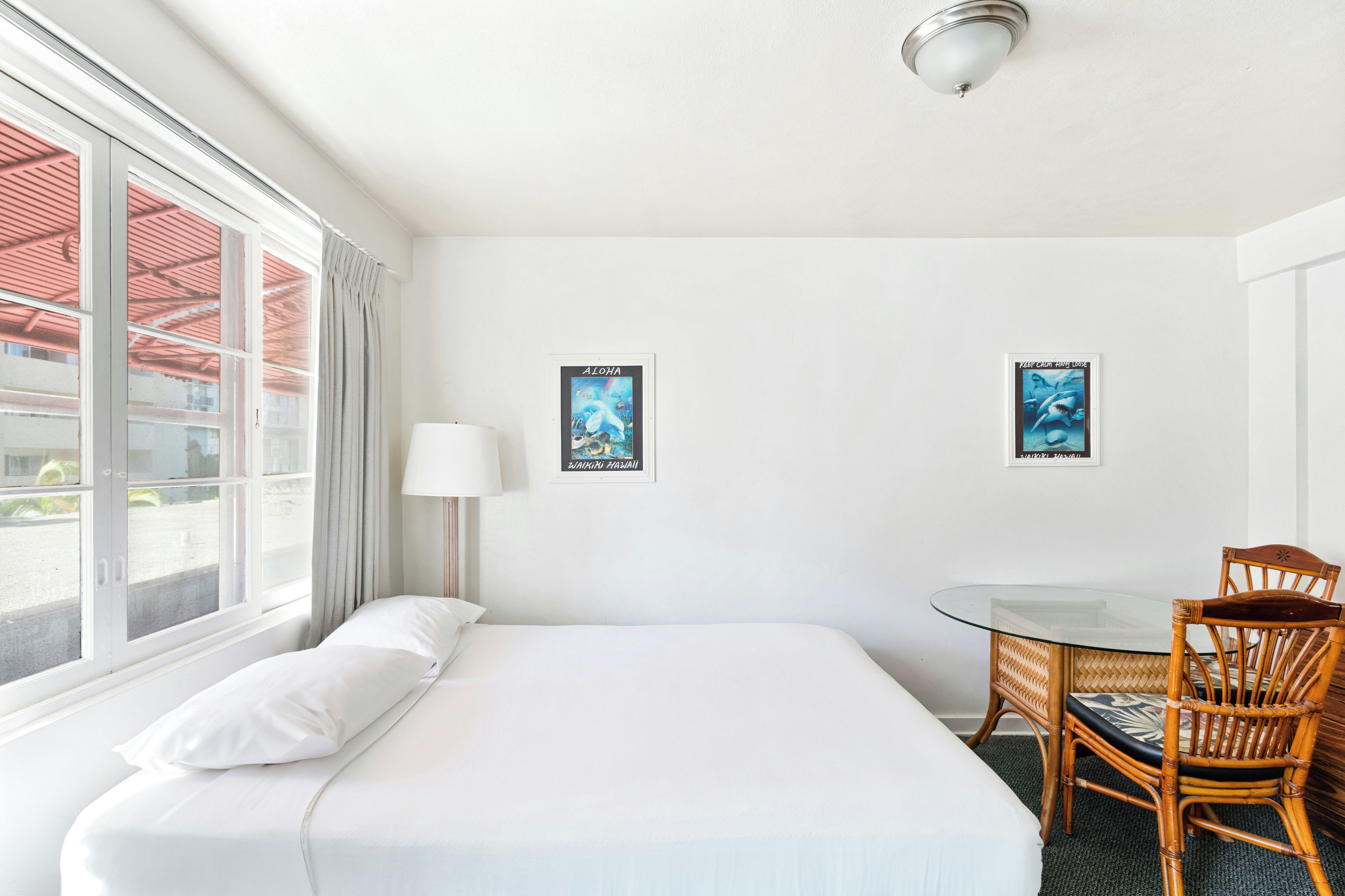 A hotel room with a bed, a desk, a chair, and two posters on the wall.