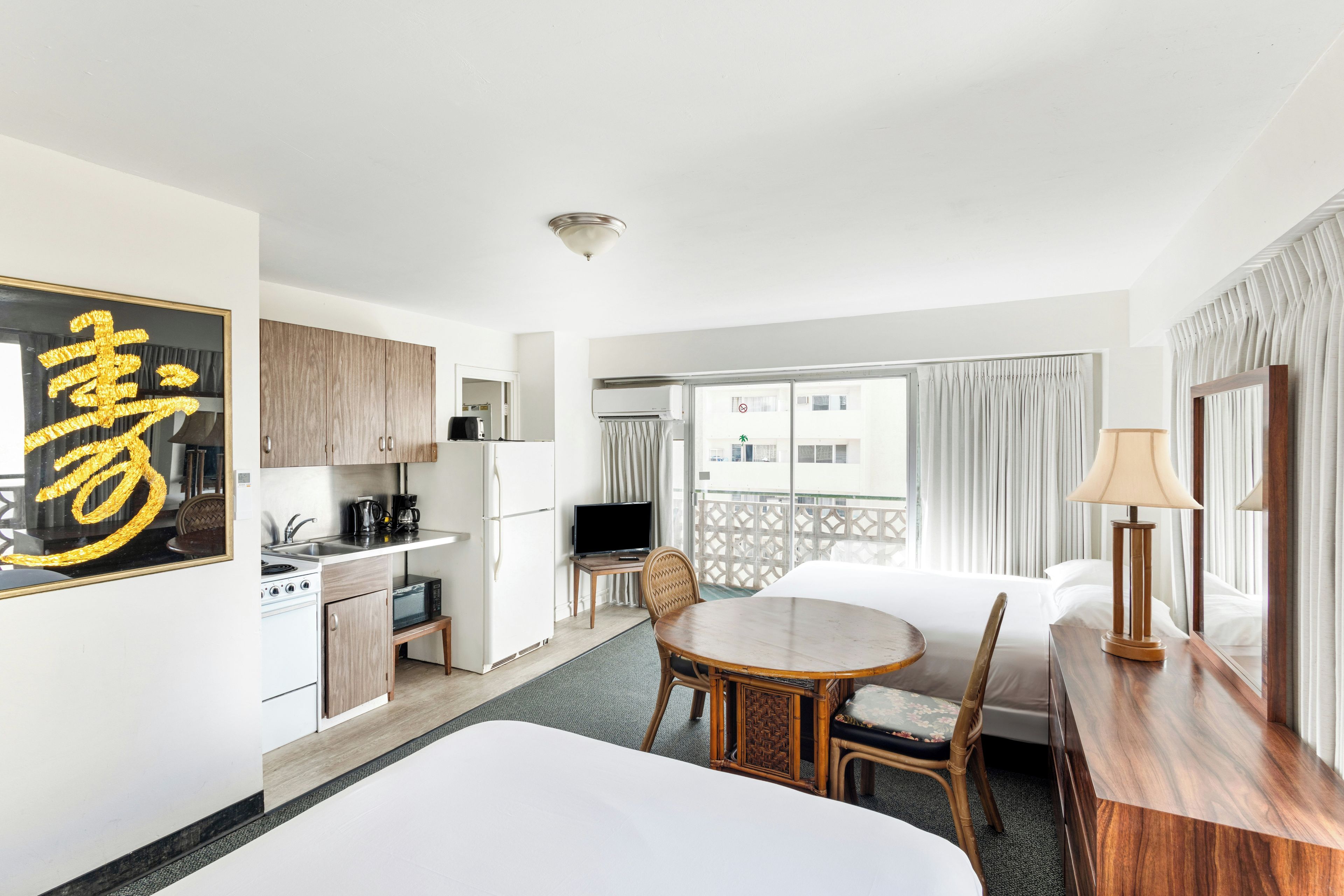 Habitación de hotel con cama, mesa de comedor, zona de cocina y balcón con cortinas.