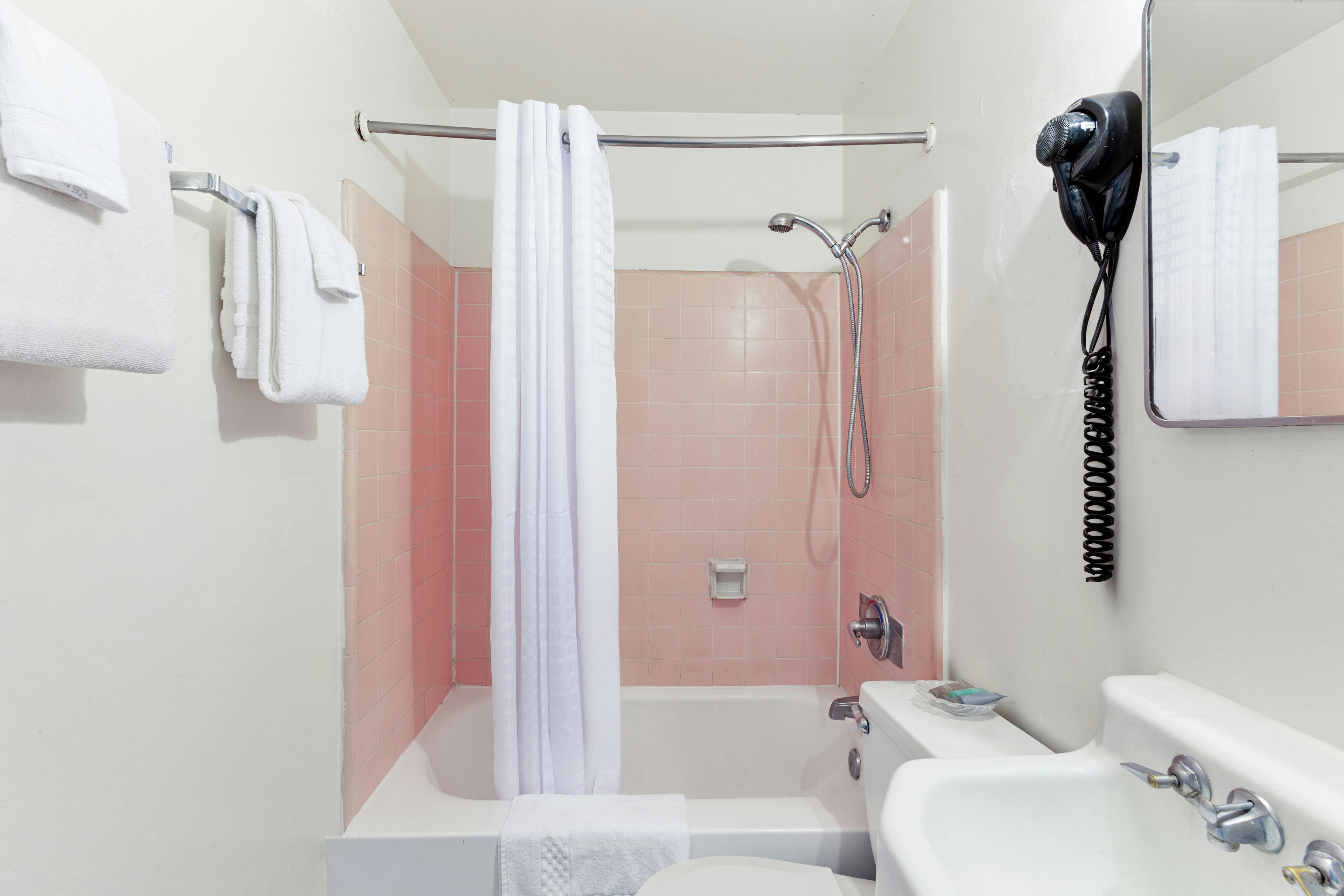 Ein Badezimmer mit einer Badewanne, einer Dusche, einem Waschbecken und einem an der Wand befestigten Föhn.