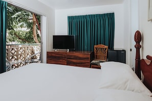 A bedroom with a bed, a dresser, a chair, a TV, and a window with curtains.