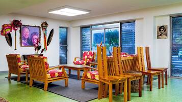 A room with wooden chairs and tables, a large window with blinds, and wall decorations including a framed photo and cultural artifacts.