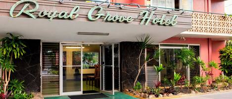 The exterior of the Royal Grove Hotel with a sign above the entrance, a stone facade, and a green lawn area.