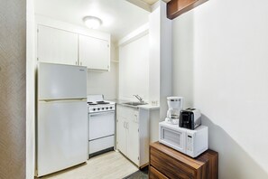 A compact kitchen with white cabinetry, a stove, a sink, and a microwave on a wooden cabinet. - Royal Grove Waikiki (Honolulu)