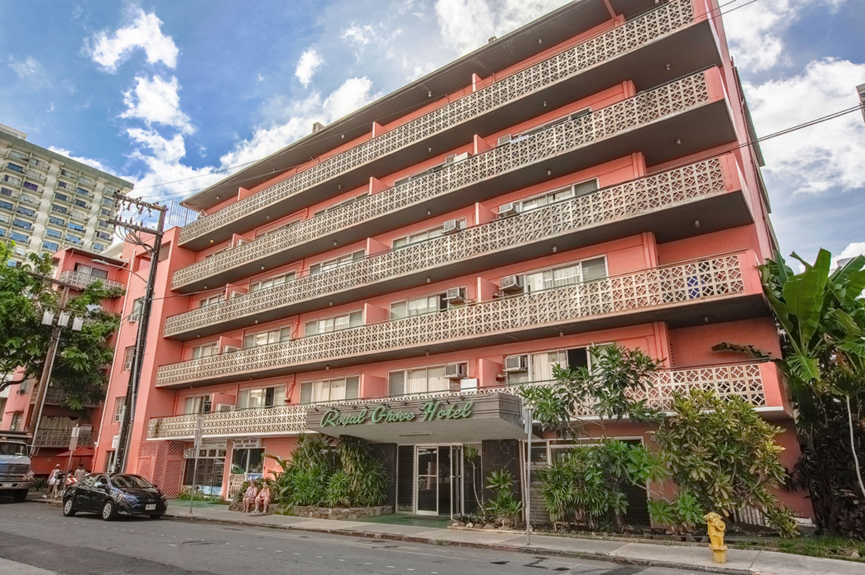 A multi-story hotel with balconies, a sign reading 'Royal Grove Hotel,' and a street view with parked cars and greenery.