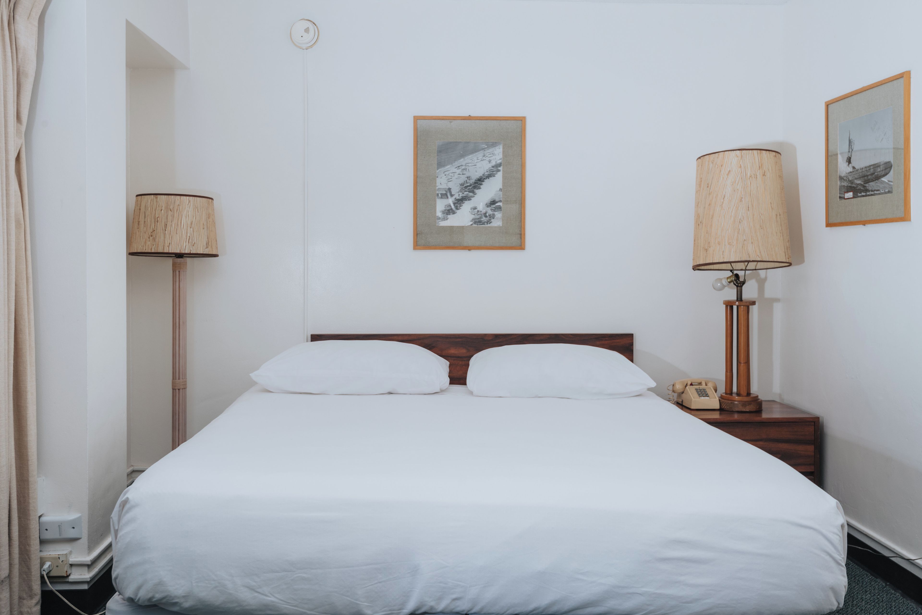Habitación de hotel con cama, dos lámparas de noche, mesita con teléfono y dos cuadros en la pared.