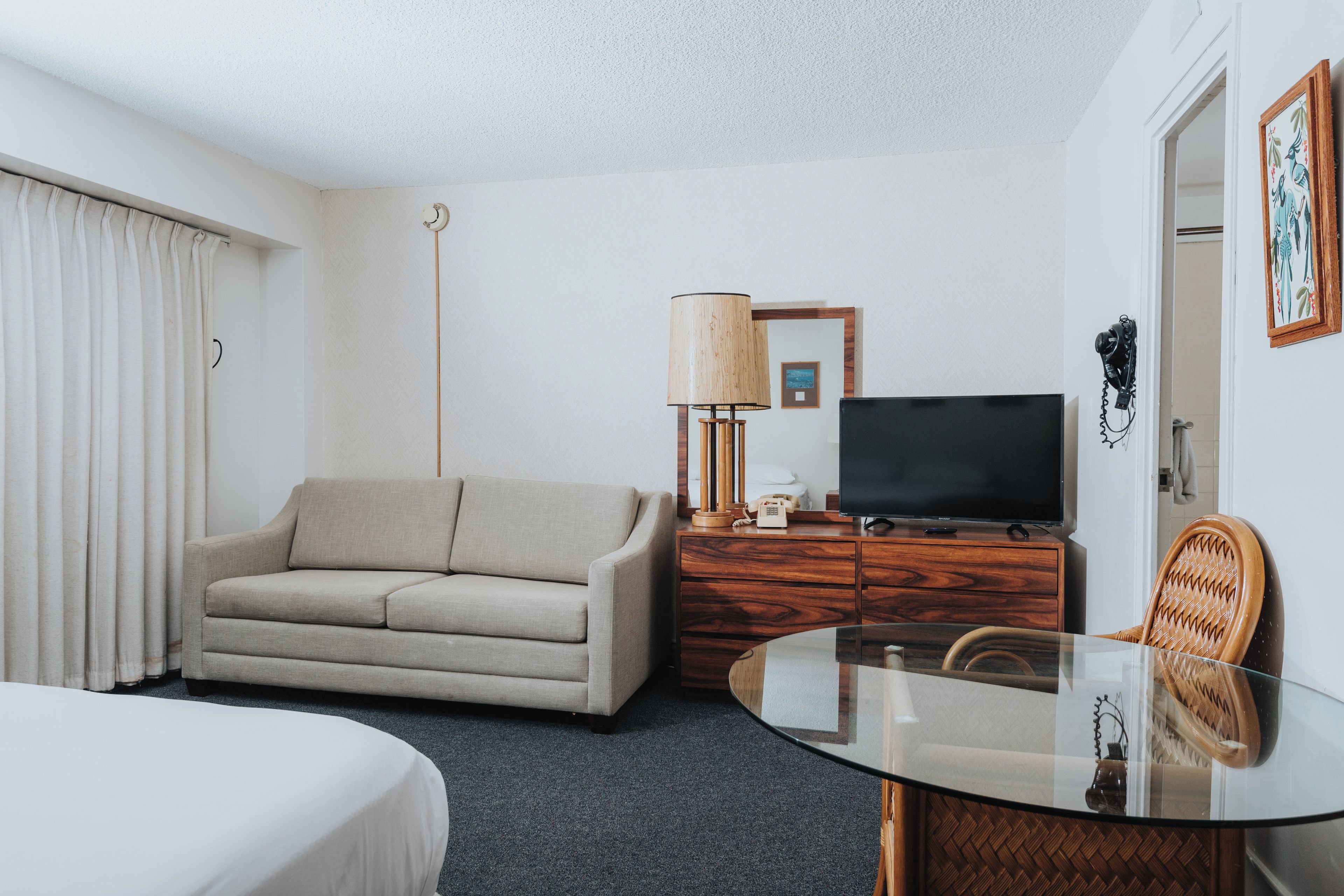 A hotel room with a bed, a sofa, a TV, a lamp, a dresser, and a chair.