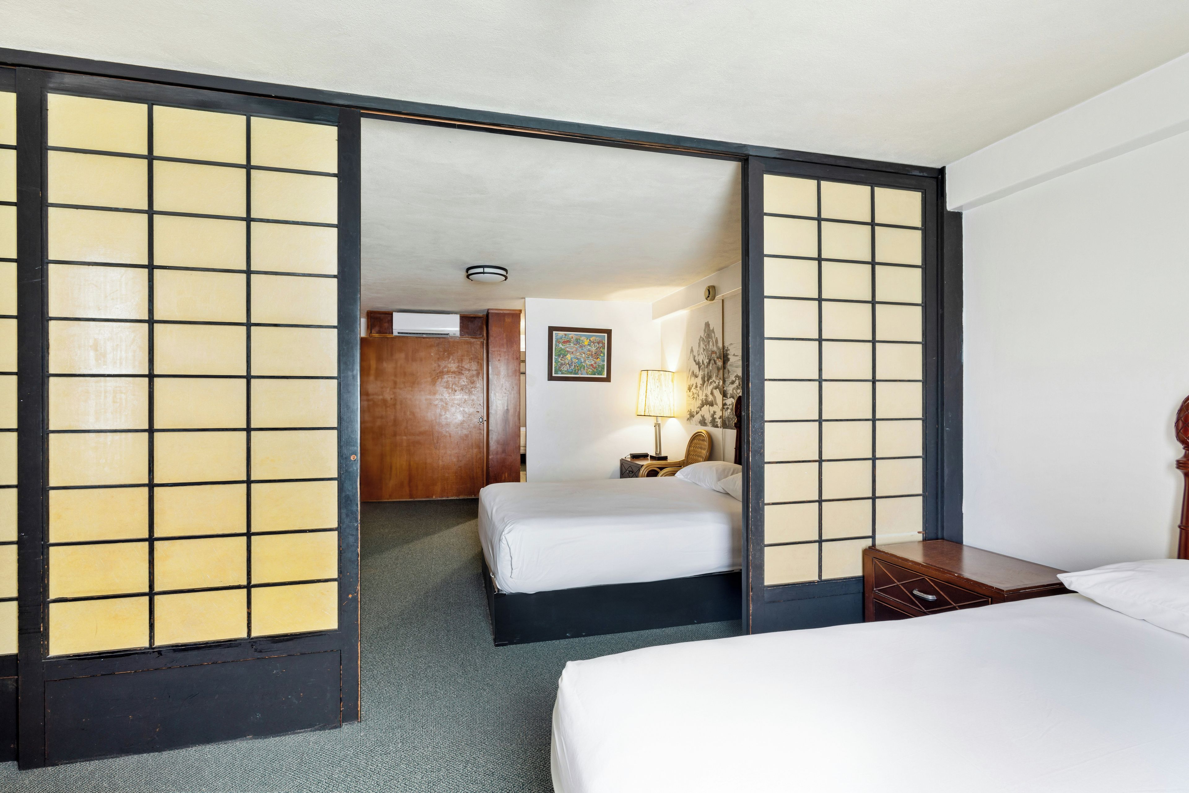 Een hotelkamer met een bed, nachtkastje, lamp en een schilderij aan de muur.