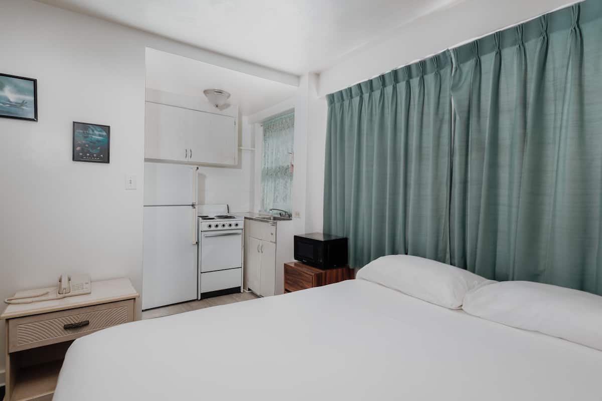 A compact hotel room with a bed, a kitchenette, a small table with a phone, and a television.
