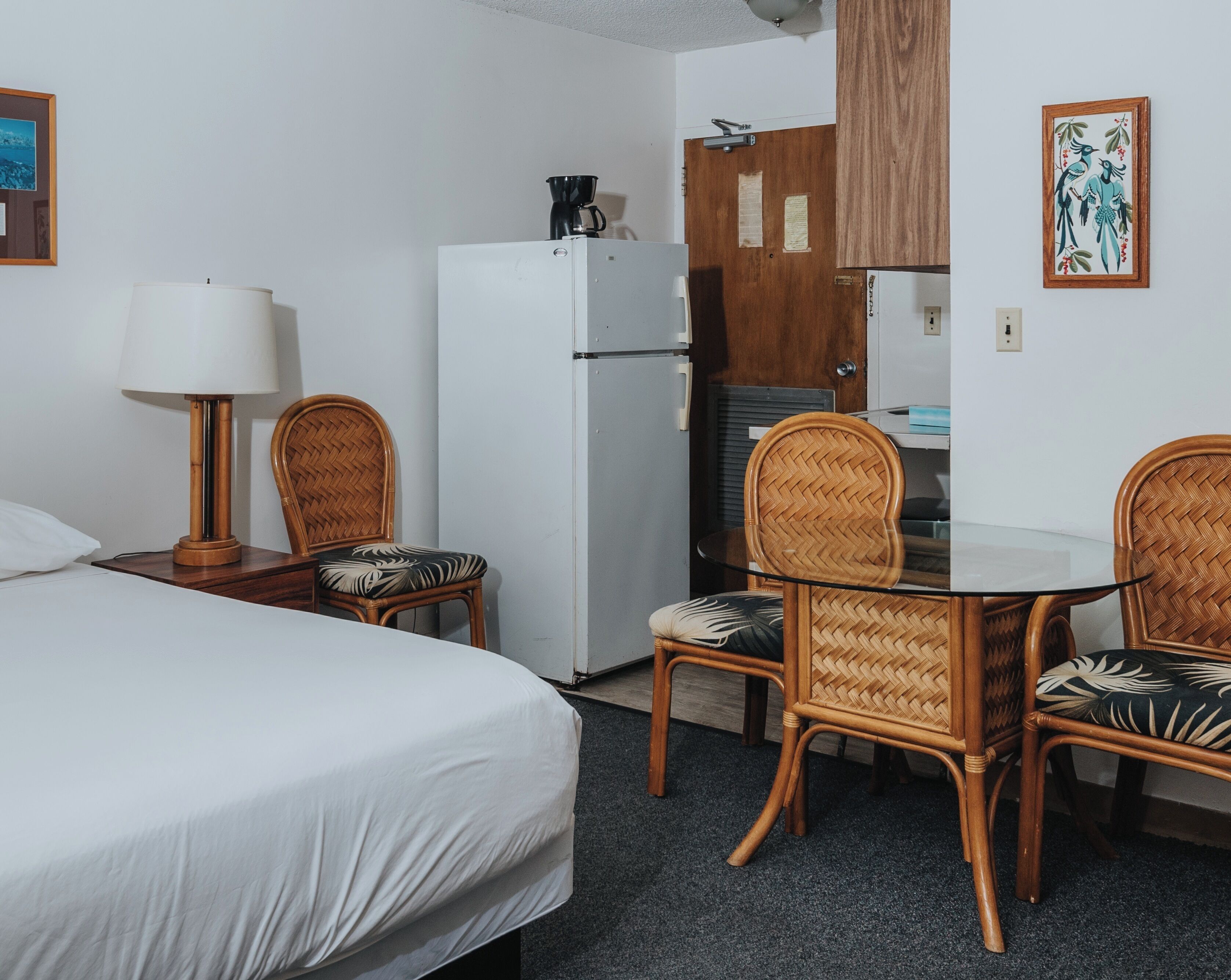 Une chambre d’hôtel comprenant un lit, une table à manger avec des chaises, un réfrigérateur, une machine à café et un meuble en bois.