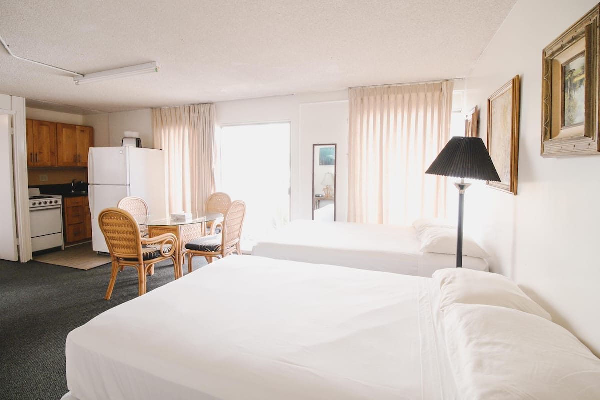 A hotel room with two beds, a dining table with chairs, a kitchenette, and a lamp.