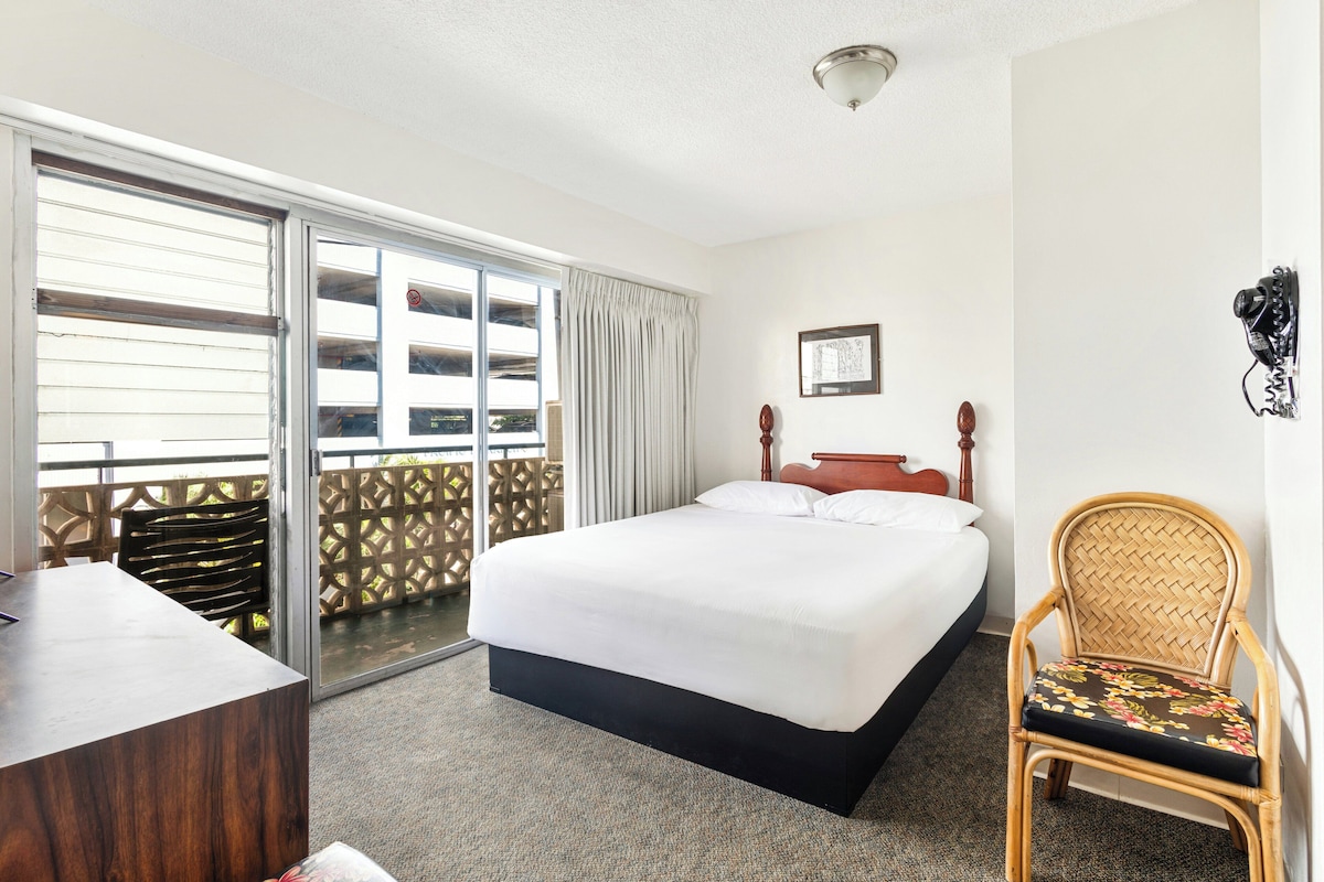 A hotel room with a bed, a desk, a chair, a window with a view, and a ceiling light.