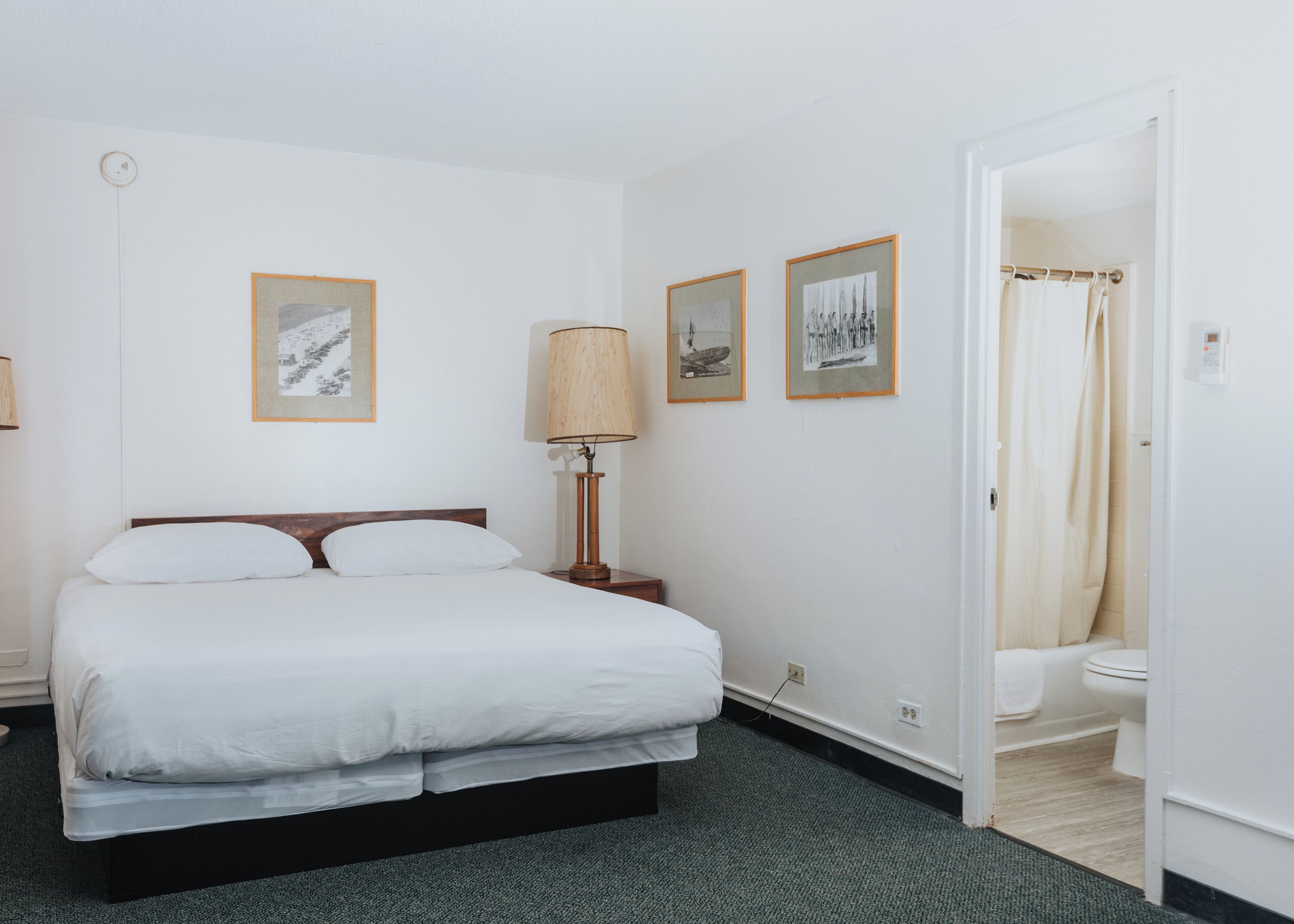 Una habitación de hotel con cama, mesita de noche, lámpara y zona de ducha.