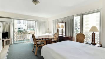 Ein Hotelzimmer mit Bett, Schreibtisch, Stuhl, Fernseher und einem Balkon mit Blick auf Gebäude, sowie einem Fenster mit Vorhängen.