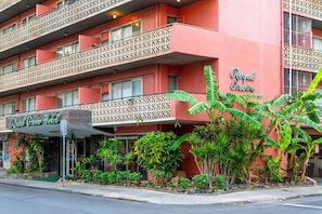 A hotel with a red facade, balconies with lattice railings, and a variety of tropical plants in the front garden. - Royal Grove Waikiki (Honolulu)