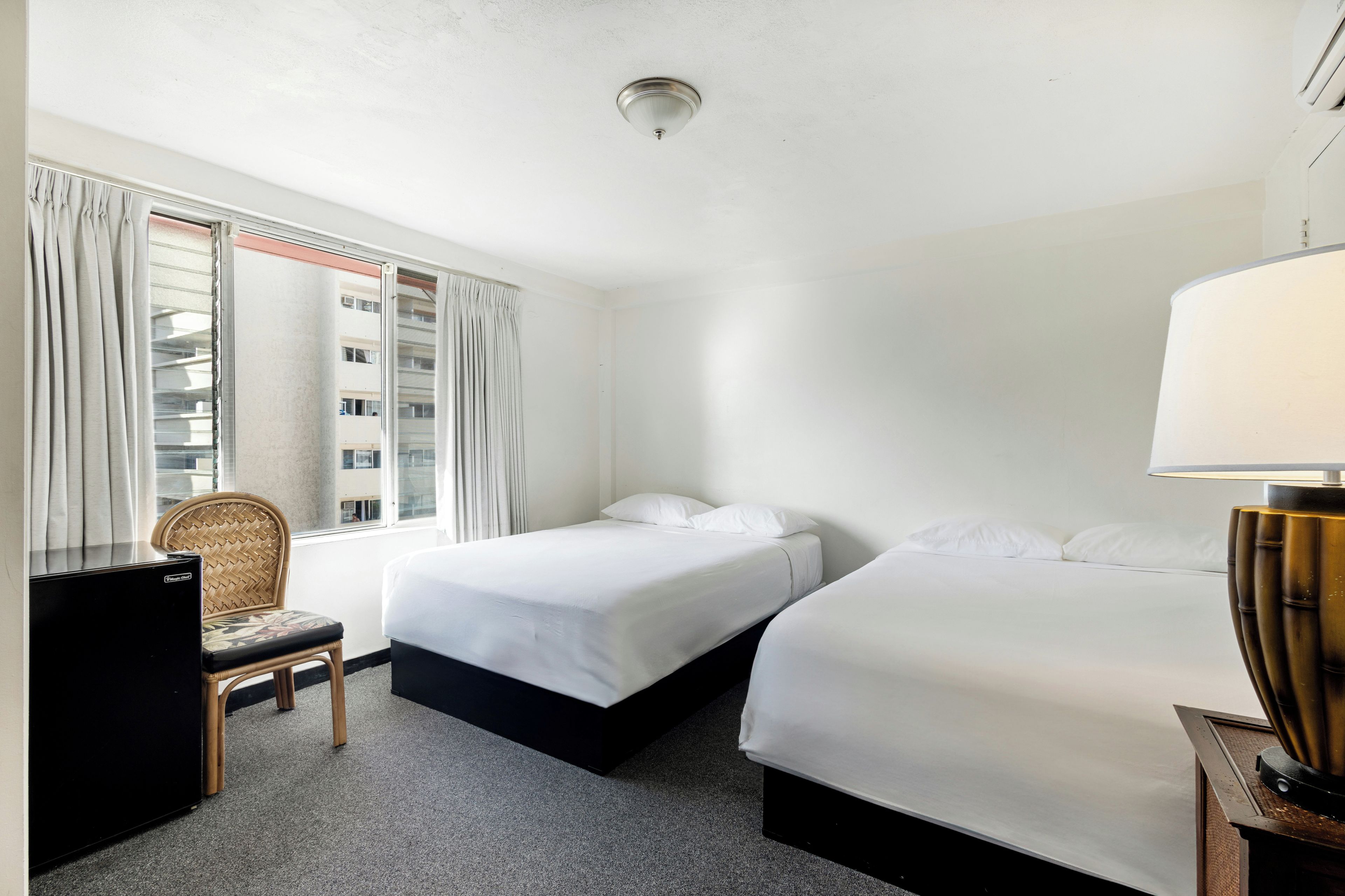 Et hotelværelse med to senge, en stol, et skrivebord og en lampe.