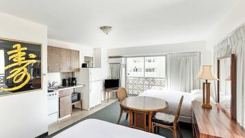 Een hotelkamer met een bed, een eettafel, een keukenhoek en een balkon met gordijnen.