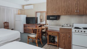 A hotel room with a bed, a desk with a chair, a kitchenette with a stove, a microwave, and a television. - Royal Grove Waikiki (Honolulu)