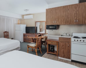 A hotel room with a bed, a desk with a chair, a kitchenette with a stove, a microwave, and a television.