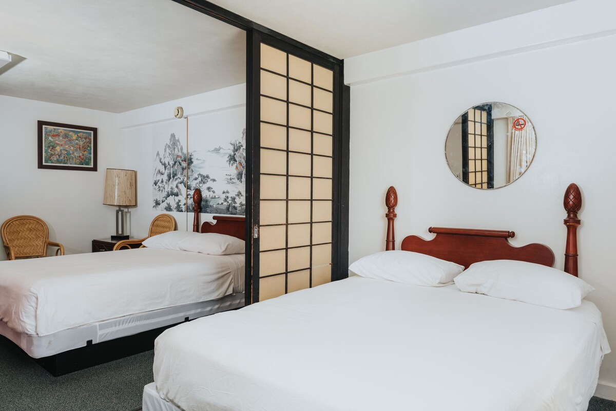 A hotel room with two beds, a traditional Japanese shoji screen, a round mirror, and a framed artwork on the wall.