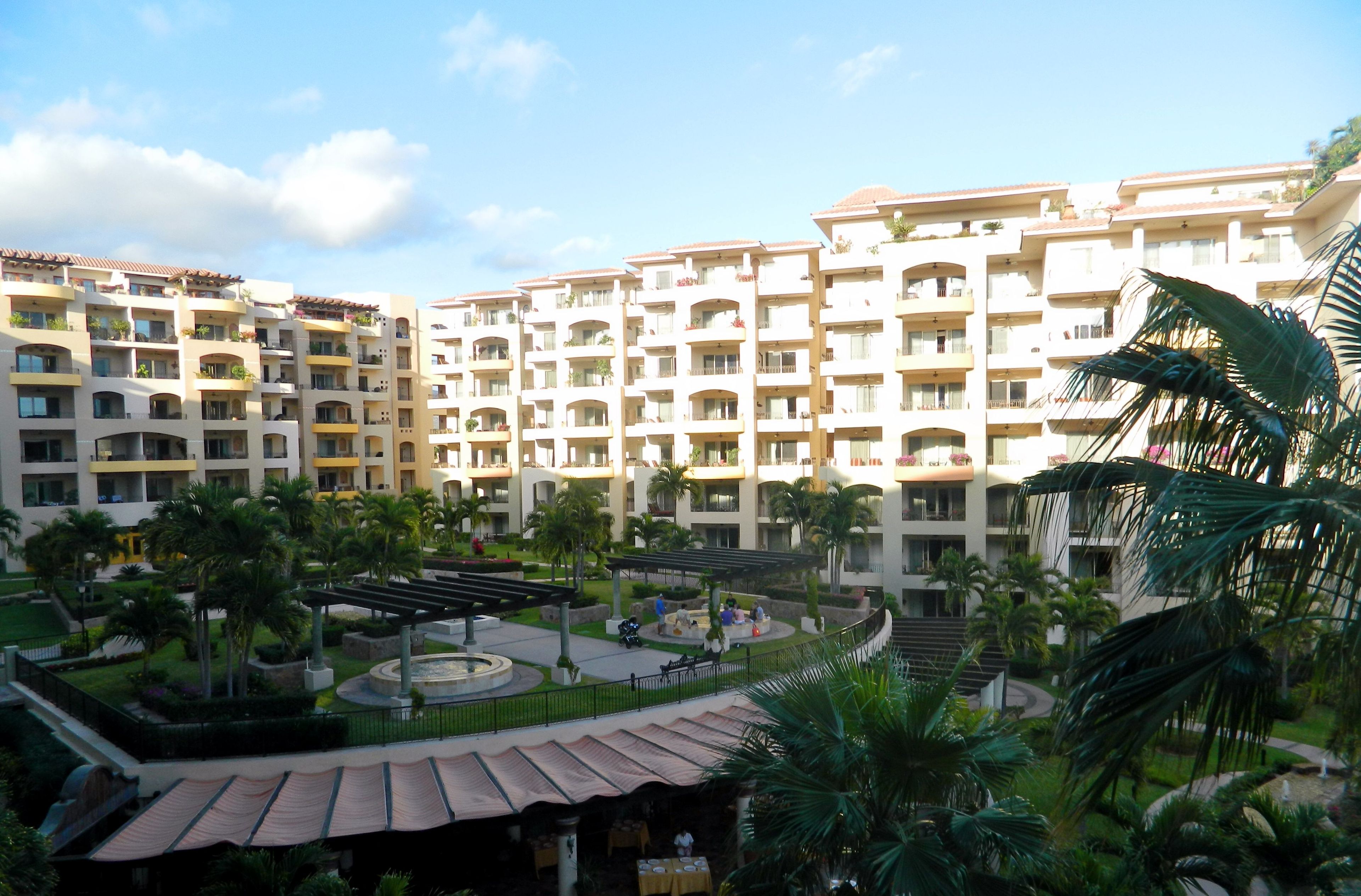 A hotel courtyard with multiple balconies, palm trees, and a central seating area.