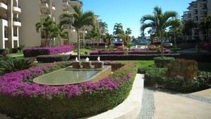 Un patio de hotel con una fuente central, rodeado de jardines cuidados y palmeras.
