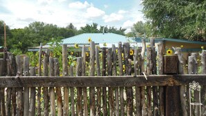 A rustic wooden fence with a metal gate, a green-roofed building, and a clear sky with clouds. -  Casita Juliet in Taos, New Mexico (Taos)