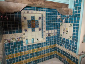 Une salle de bain avec des carreaux de mosaïque bleus et blancs, une baignoire, une douche et une poutre en bois au plafond.