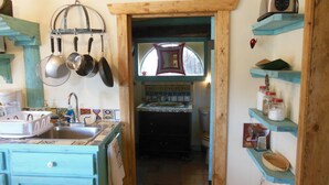 A rustic kitchen with a wooden door leading to a dining area, a sink with dishes, and hanging pots. -  Casita Juliet in Taos, New Mexico (Taos)